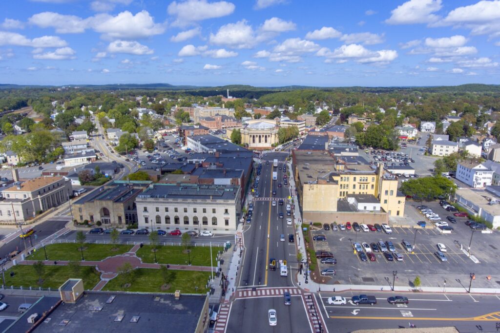 Aerial view of downtown Framingham, Massachusetts, a growing hub for biotech and life sciences innovation, showing city streets, historic buildings, and surrounding green areas under a bright blue sky.