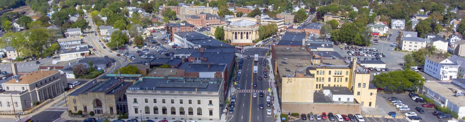 Aerial view of downtown Framingham, Massachusetts, a growing hub for biotech and life sciences innovation, showing city streets, historic buildings, and surrounding green areas under a bright blue sky.